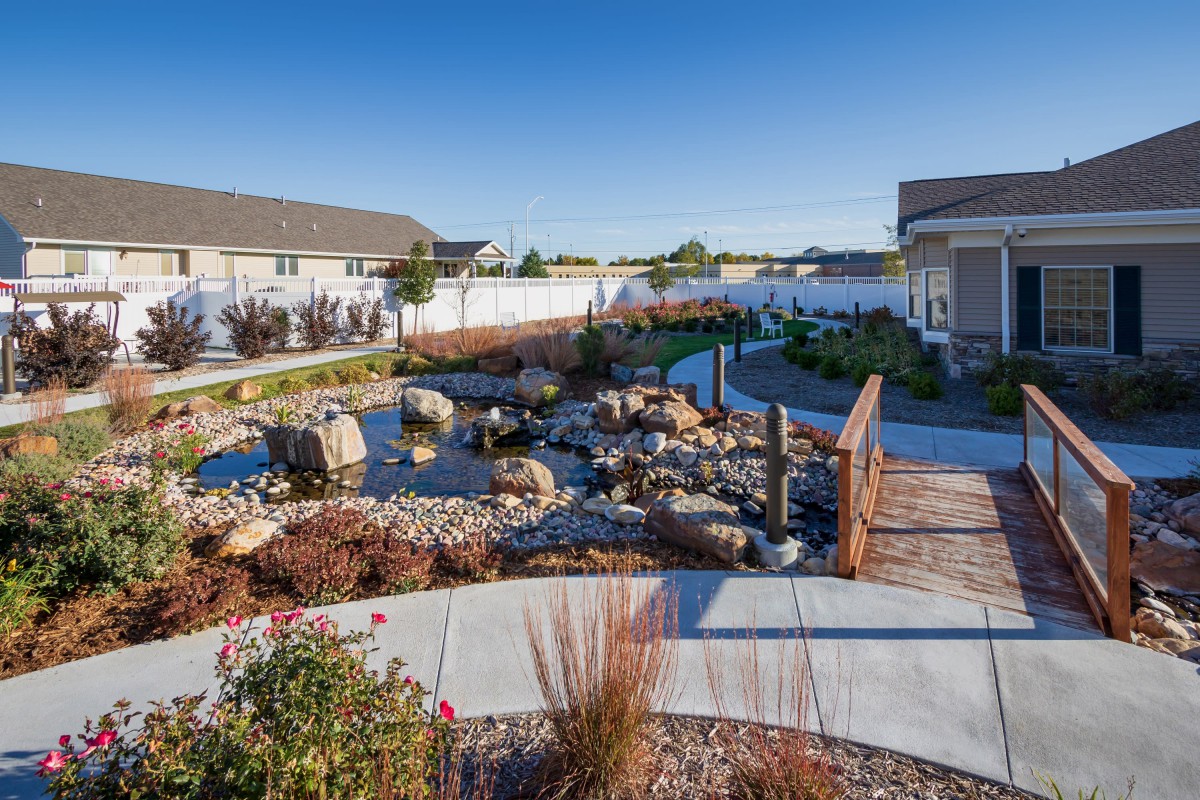 A beautifully landscaped garden with a pond, rocks, and a wooden bridge in a residential area.