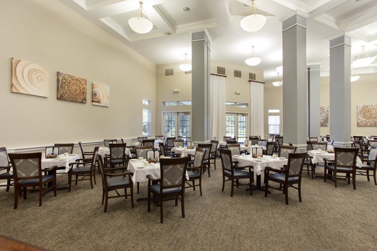 An elegant dining room with neatly arranged tables and chairs, featuring white tablecloths and ambient lighting.