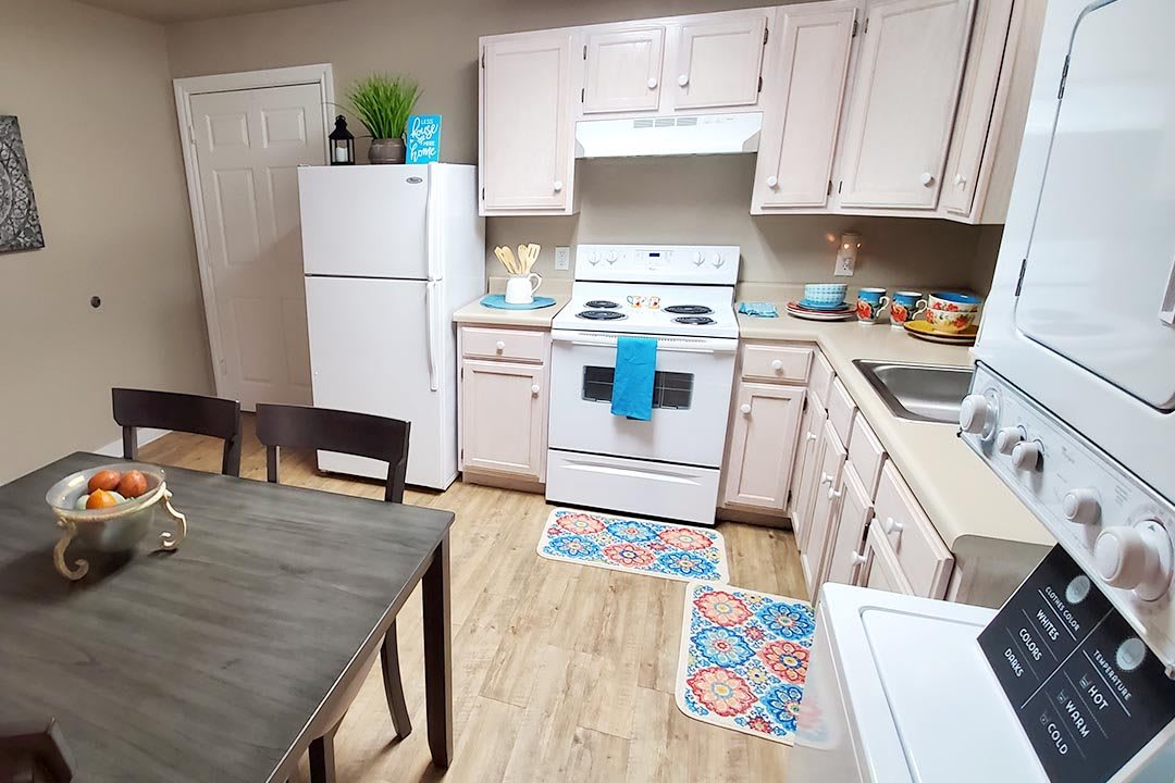A cozy kitchen with white cabinets and appliances, featuring a dining table and colorful decor.