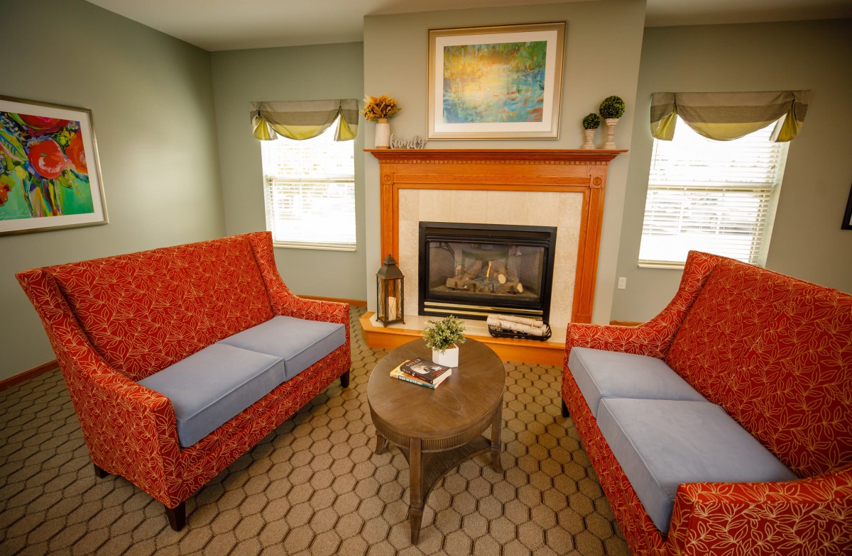 A cozy living room featuring a fireplace, two red couches, and a central wooden coffee table.