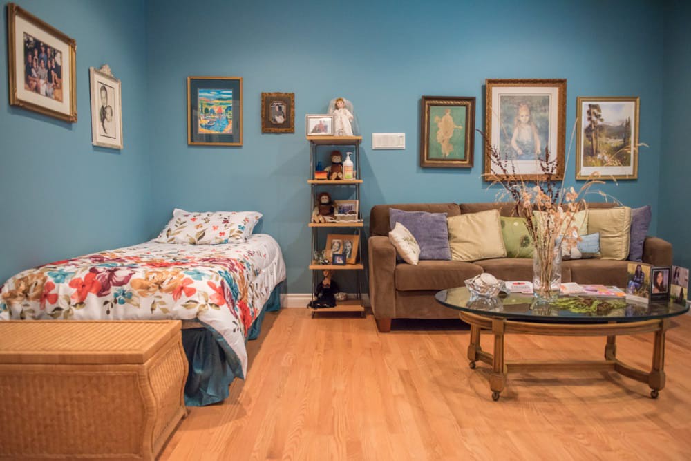 A cozy living space featuring a bed with a floral duvet, a comfortable sofa with cushions, and artwork adorning the blue walls.