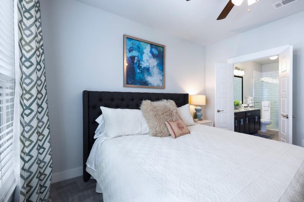 A cozy bedroom with a neatly made bed, adorned with cushions and a modern artwork above the headboard.