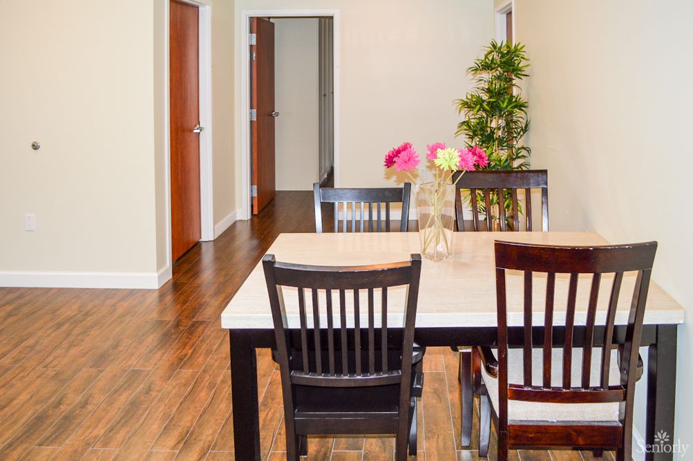 A modern dining room with a wooden table and chairs, adorned with a vase of pink flowers and featuring hardwood flooring.