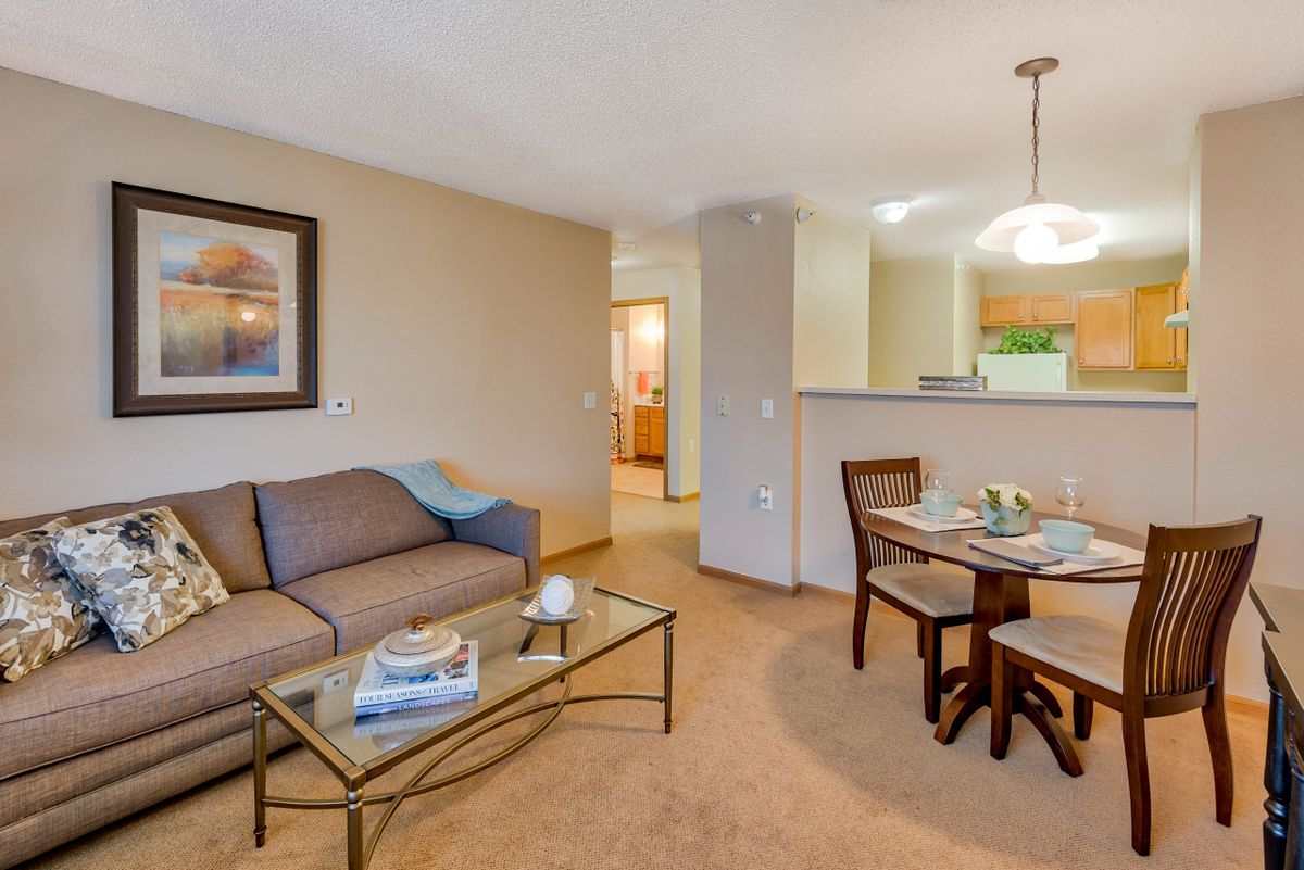 A cozy apartment interior featuring a comfortable living room with a sofa and a small dining area with a table and chairs.
