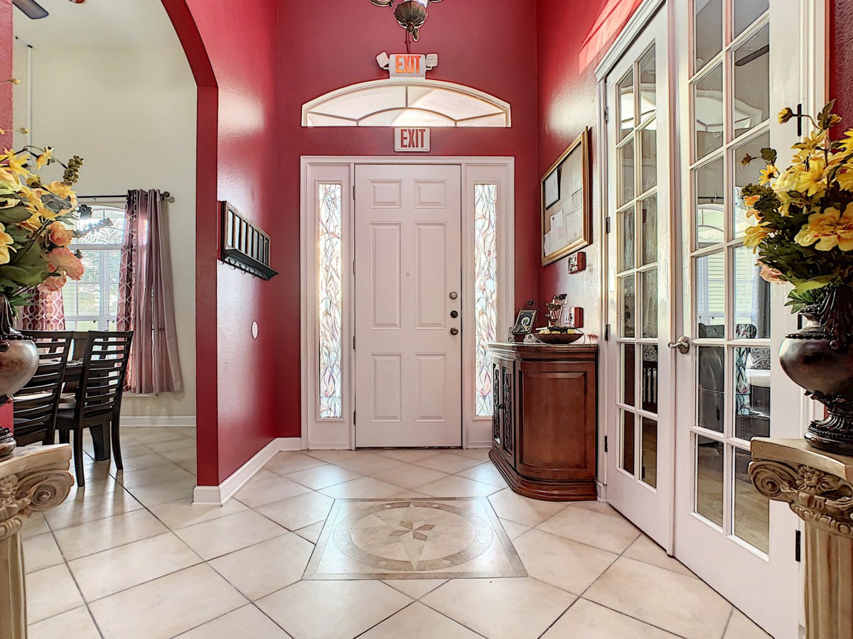 A traditional entryway with red walls, a white front door, and tile flooring.