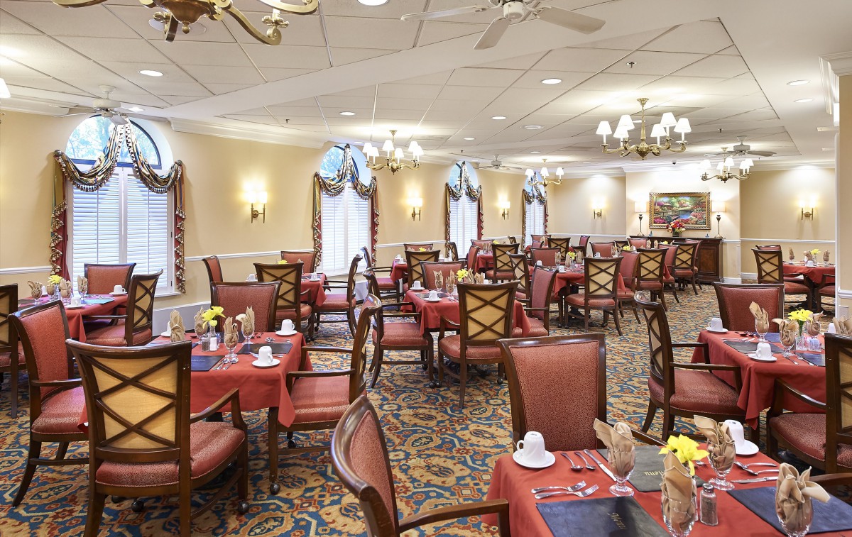 An elegant dining room with neatly arranged tables and chairs, featuring chandeliers and a carpeted floor.
