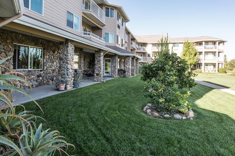 A well-maintained lawn in front of an apartment building with stone columns and balconies.