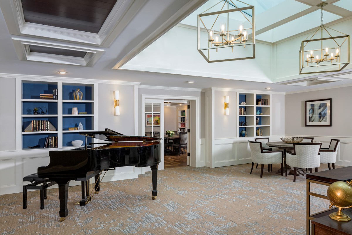 A modern living area featuring a grand piano, stylish chandelier, and built-in bookshelves.