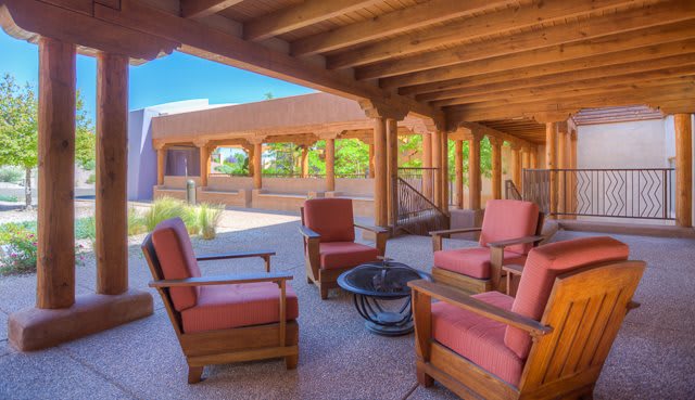 A cozy outdoor patio with wooden chairs and a fire pit under a covered terrace.