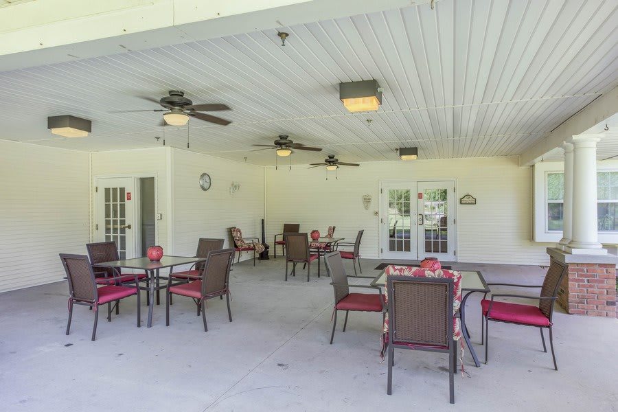 An outdoor patio with multiple tables and chairs under a covered roof, featuring ceiling fans for comfort.