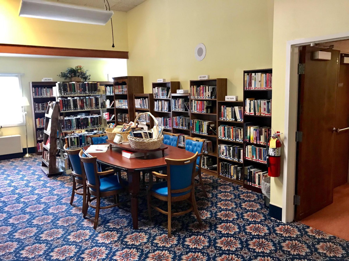 A cozy library corner with shelves filled with books surrounding a table and chairs on a patterned carpet.