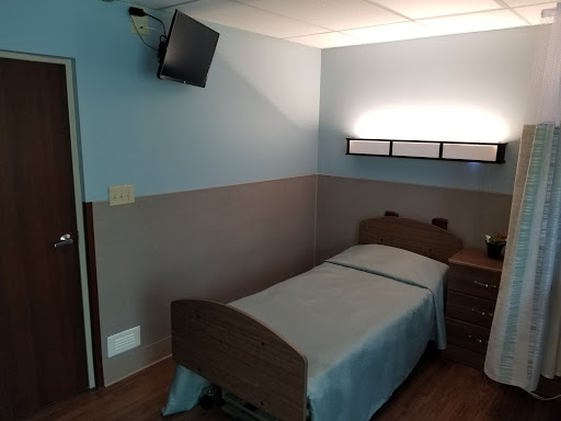 A simple hospital room featuring a single bed and a wall-mounted television.