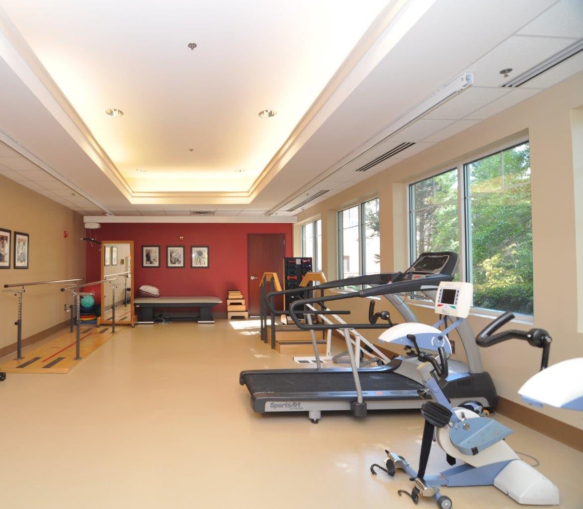 A well-equipped gym with exercise machines including treadmills and stationary bikes next to large windows.