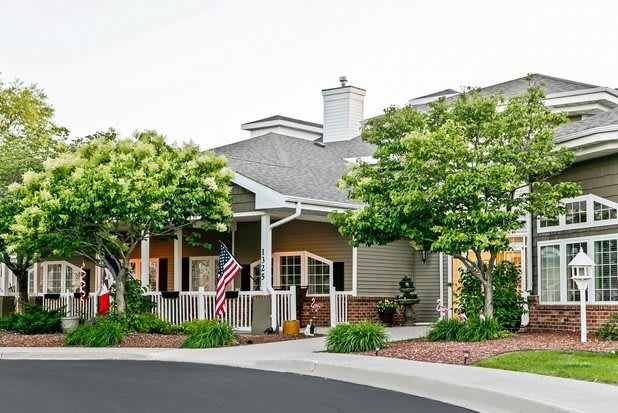 A charming residential house with a front porch and an American flag, surrounded by trees and greenery.