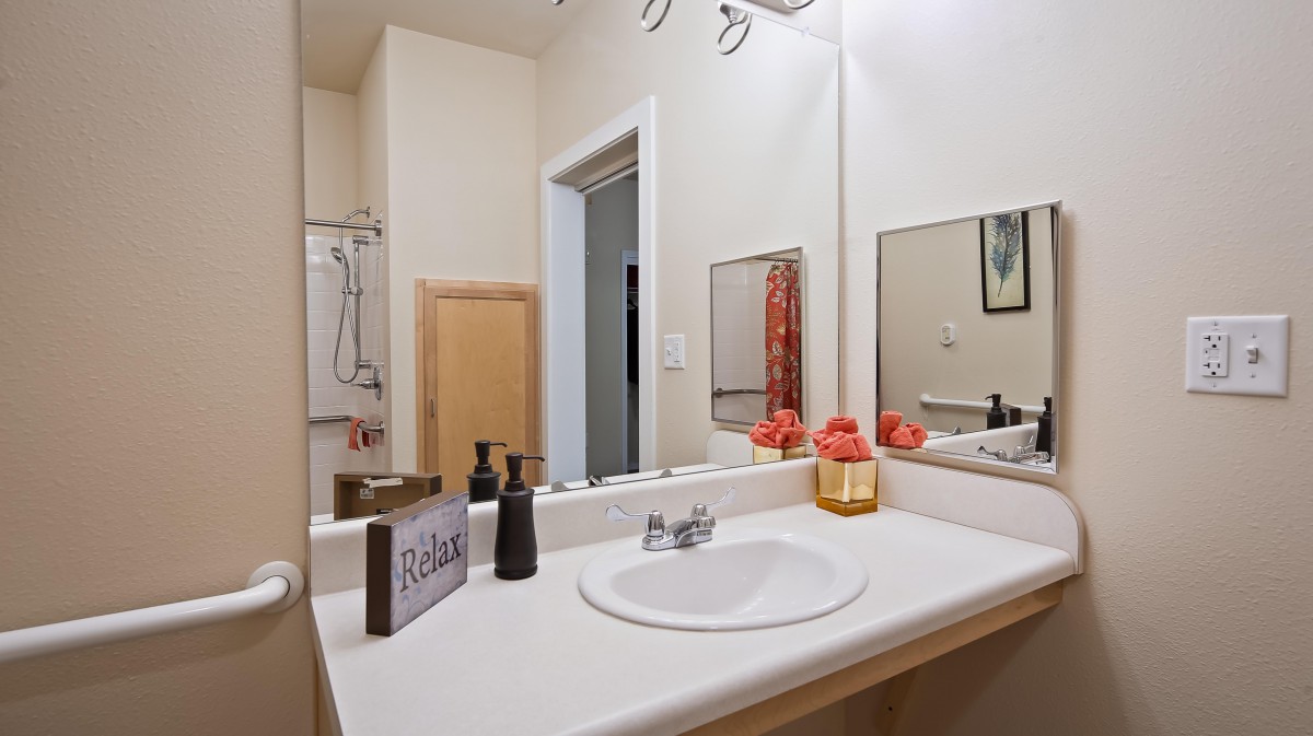 A clean and tidy bathroom with a sink, mirror, soap dispenser, and neatly arranged towels.