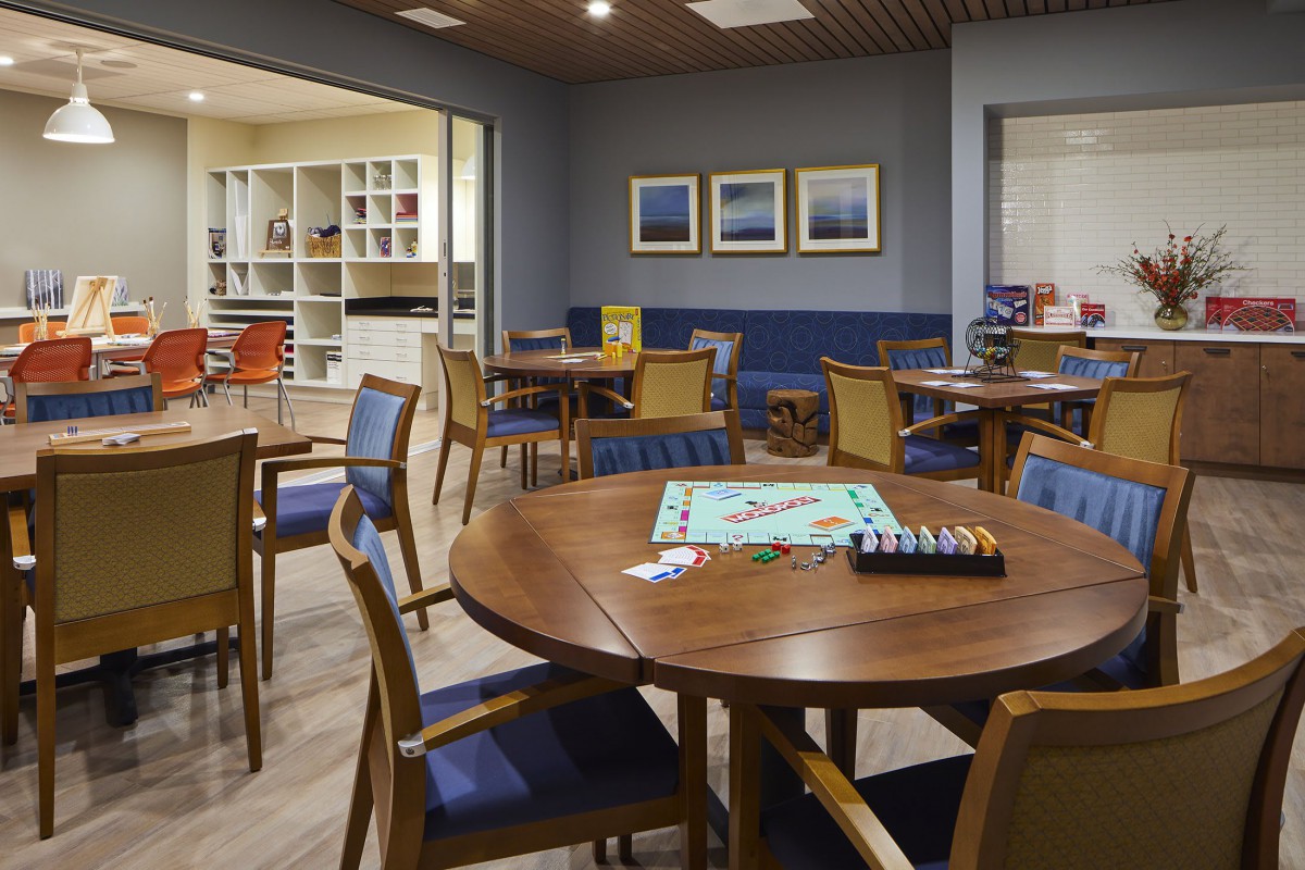 A modern game room featuring multiple tables with board games, surrounded by chairs and shelves.