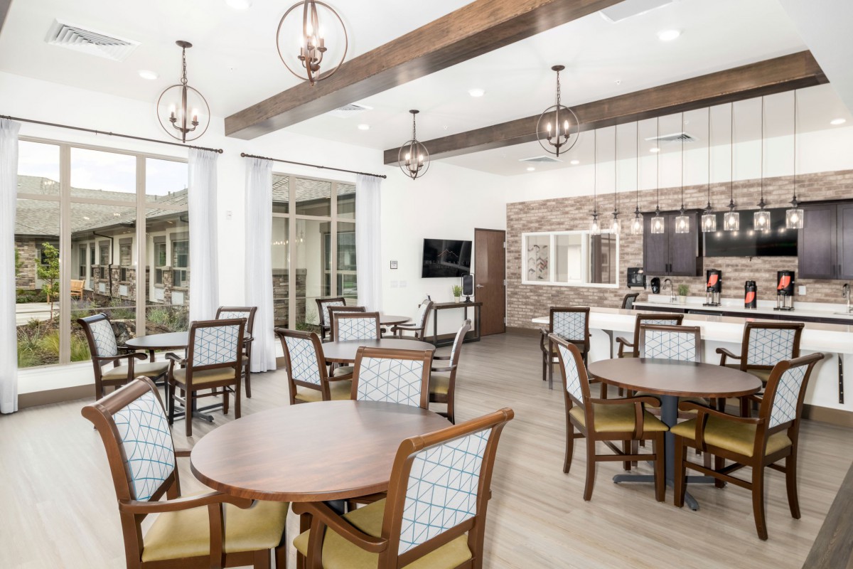 A modern dining area with wooden tables and chairs, featuring ceiling lights and large windows.