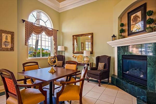 A elegantly decorated living room featuring a dining table and chairs, a cozy armchair by the fireplace, large windows, and tasteful decor.