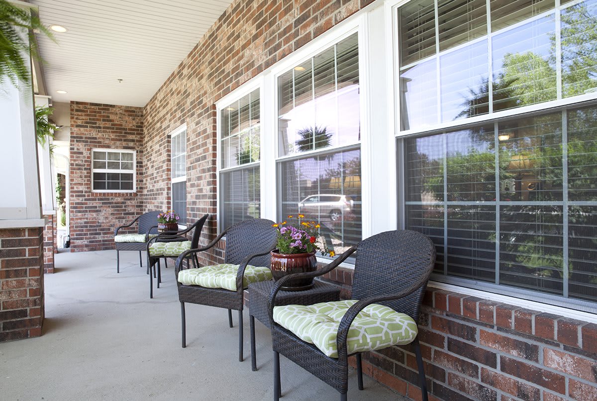 A cozy porch with wicker chairs and plants against a brick wall.