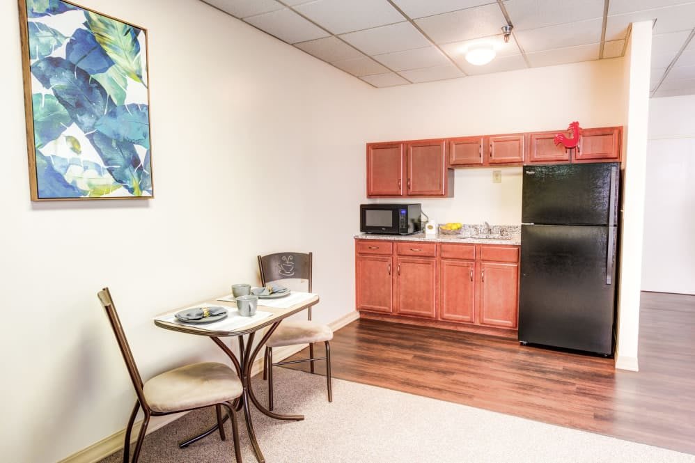 A compact kitchen and dining area with a table, chairs, microwave, refrigerator, and cabinets.