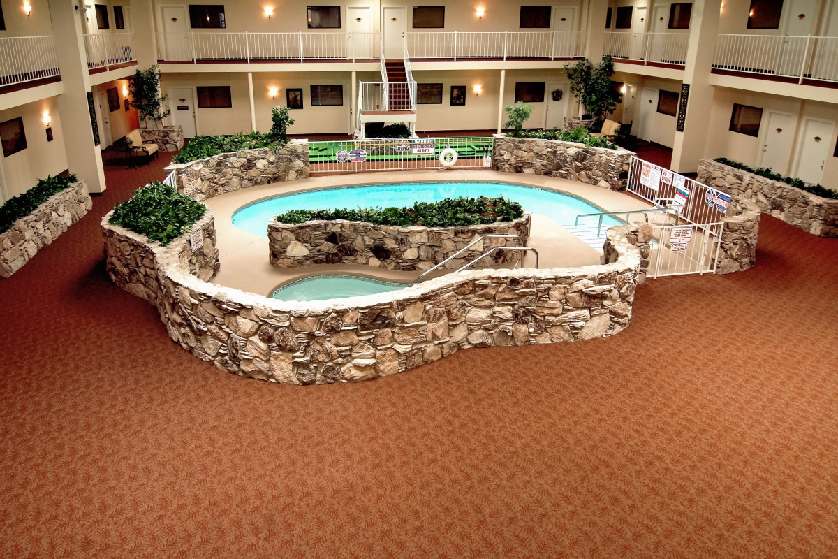 An indoor swimming pool area within a hotel atrium, featuring stone accents and lush greenery.