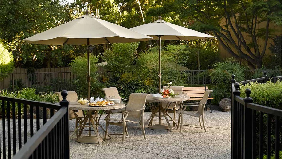 A serene outdoor patio setting with tables, chairs, and umbrellas surrounded by lush greenery.