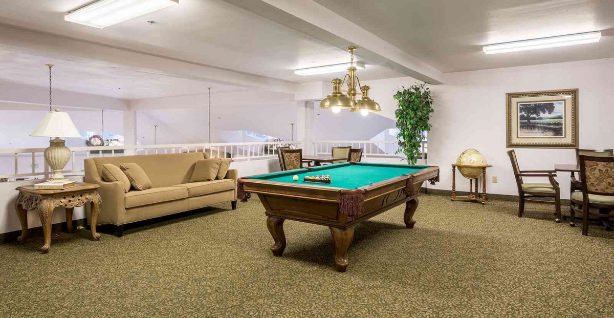 A cozy lounge area featuring a pool table under elegant lighting, complemented by comfortable seating.