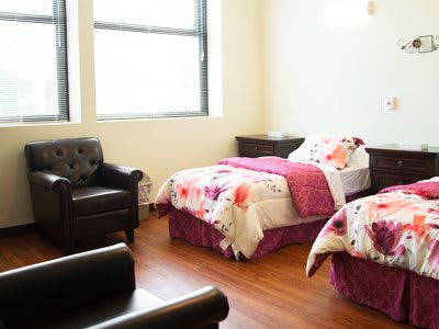A cozy bedroom with twin beds, floral bedding, and an armchair by the window.