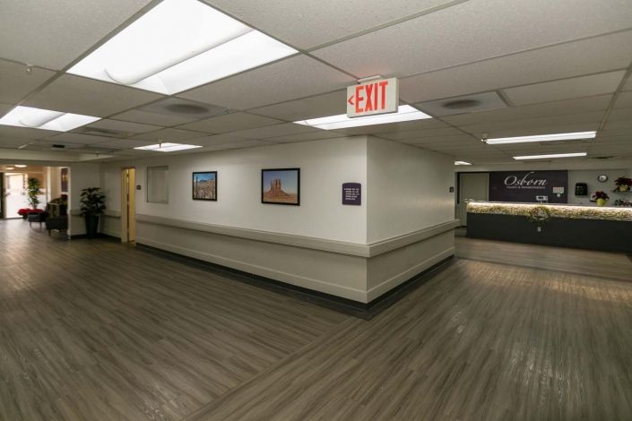 A hospital corridor with artwork on the walls and an exit sign overhead.