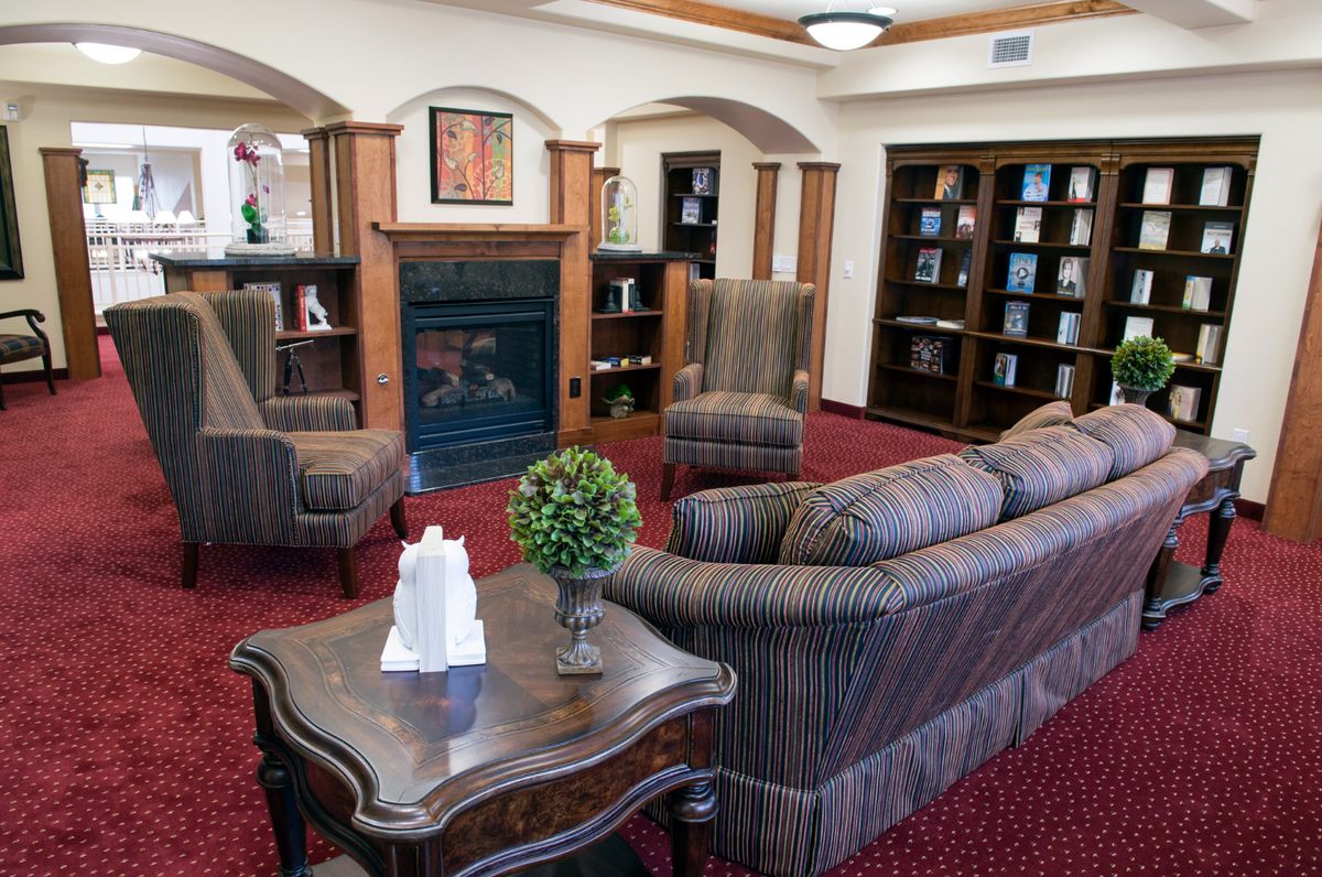 A cozy living room with a fireplace, sofas, armchairs, and bookshelves.