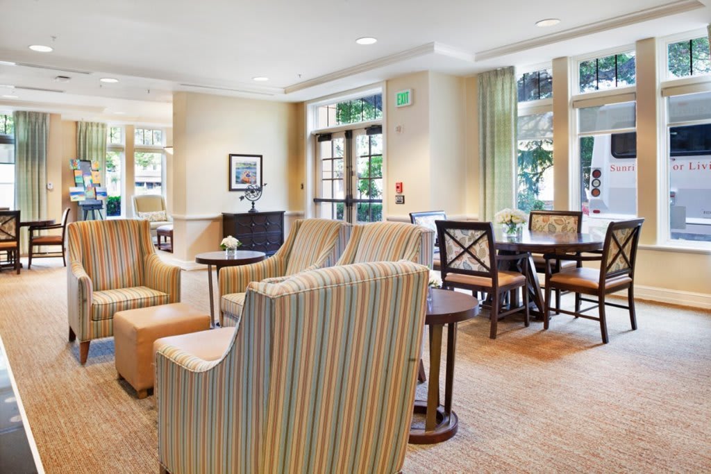 A bright and inviting seating area with comfortable chairs and tables, accented by large windows and light-colored decor.