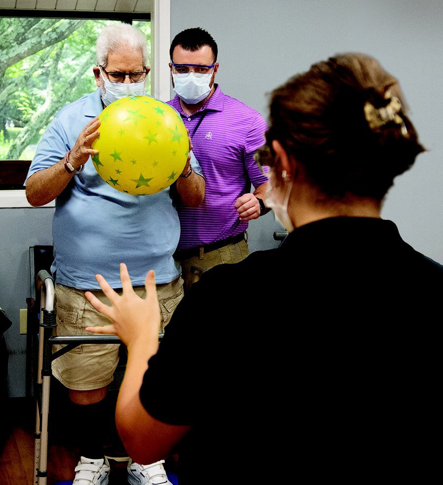 A physical therapy session where a patient is engaging in an exercise with the assistance of healthcare professionals.