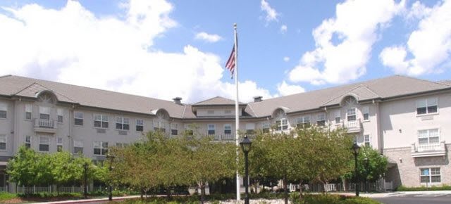 A building with a flagpole in front, surrounded by trees under a partly cloudy sky.
