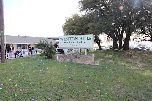 A sign for Western Hills, situated in a grassy area with trees nearby.