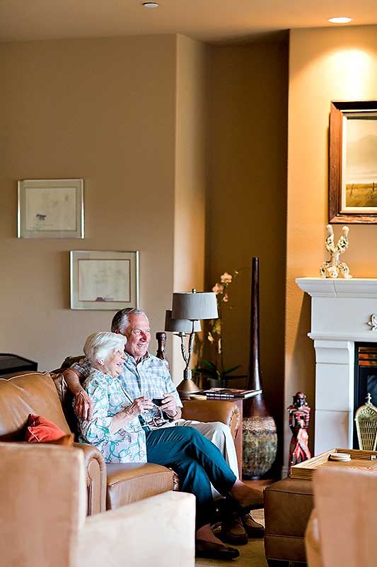 An older couple sitting together on a couch in a warmly decorated living room.