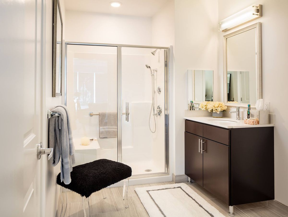 A modern bathroom featuring a glass-enclosed shower, a dark wood vanity with a large mirror, and minimalist decor.