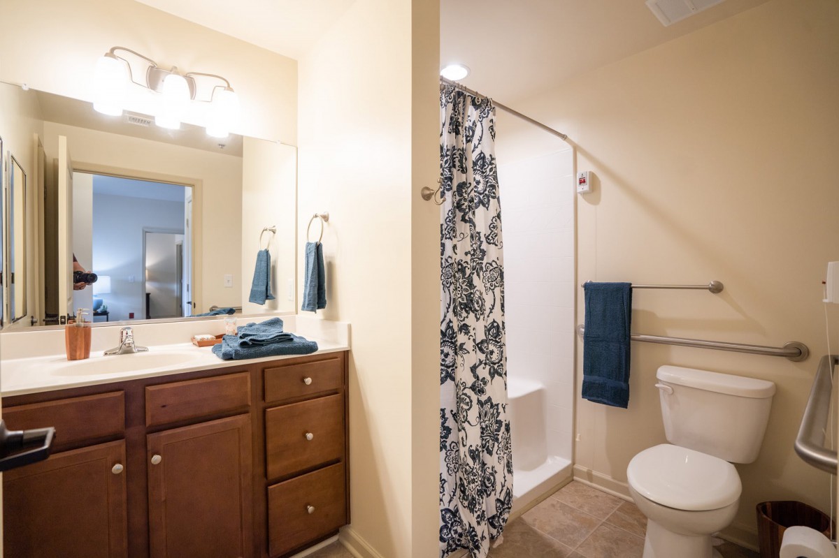 A modern bathroom featuring a sink with a mirror and cabinet, a shower with a patterned curtain, and neatly arranged towels.