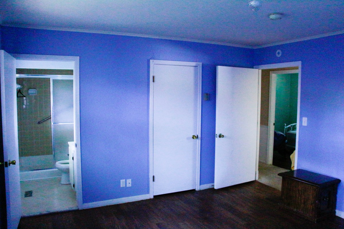 A room with blue walls, white doors, and dark wood flooring, featuring a view into an adjacent bathroom.