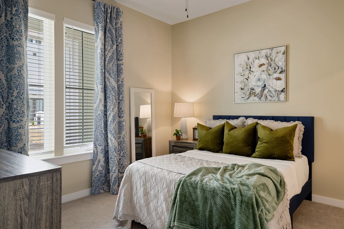 A cozy bedroom with elegant decor, featuring a bed adorned with green pillows and blanket, a bedside lamp, and artwork on the wall.