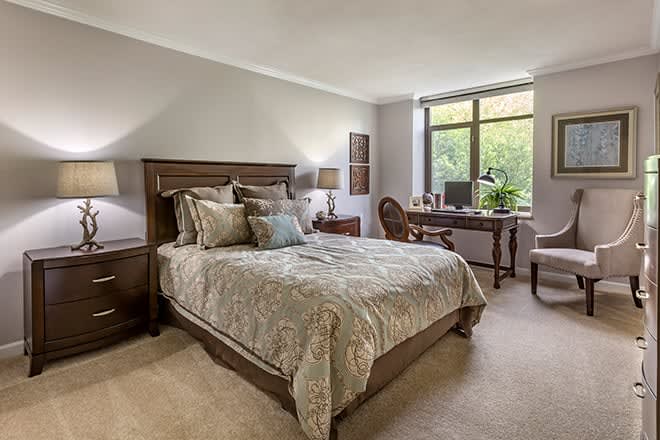 A well-furnished bedroom with a bed, desk, and large window providing natural light.