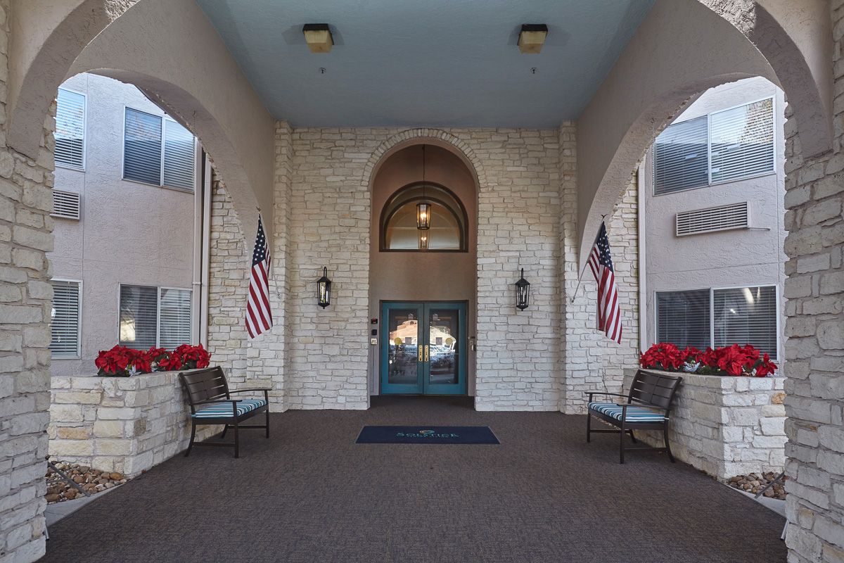 A building entrance featuring stone walls, an arched doorway, and American flags on either side.
