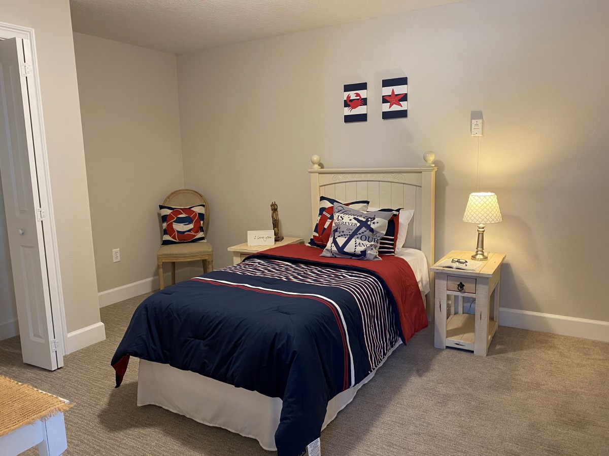A cozy bedroom with a single bed featuring striped bedding, a nightstand with a lamp, and simple decor.