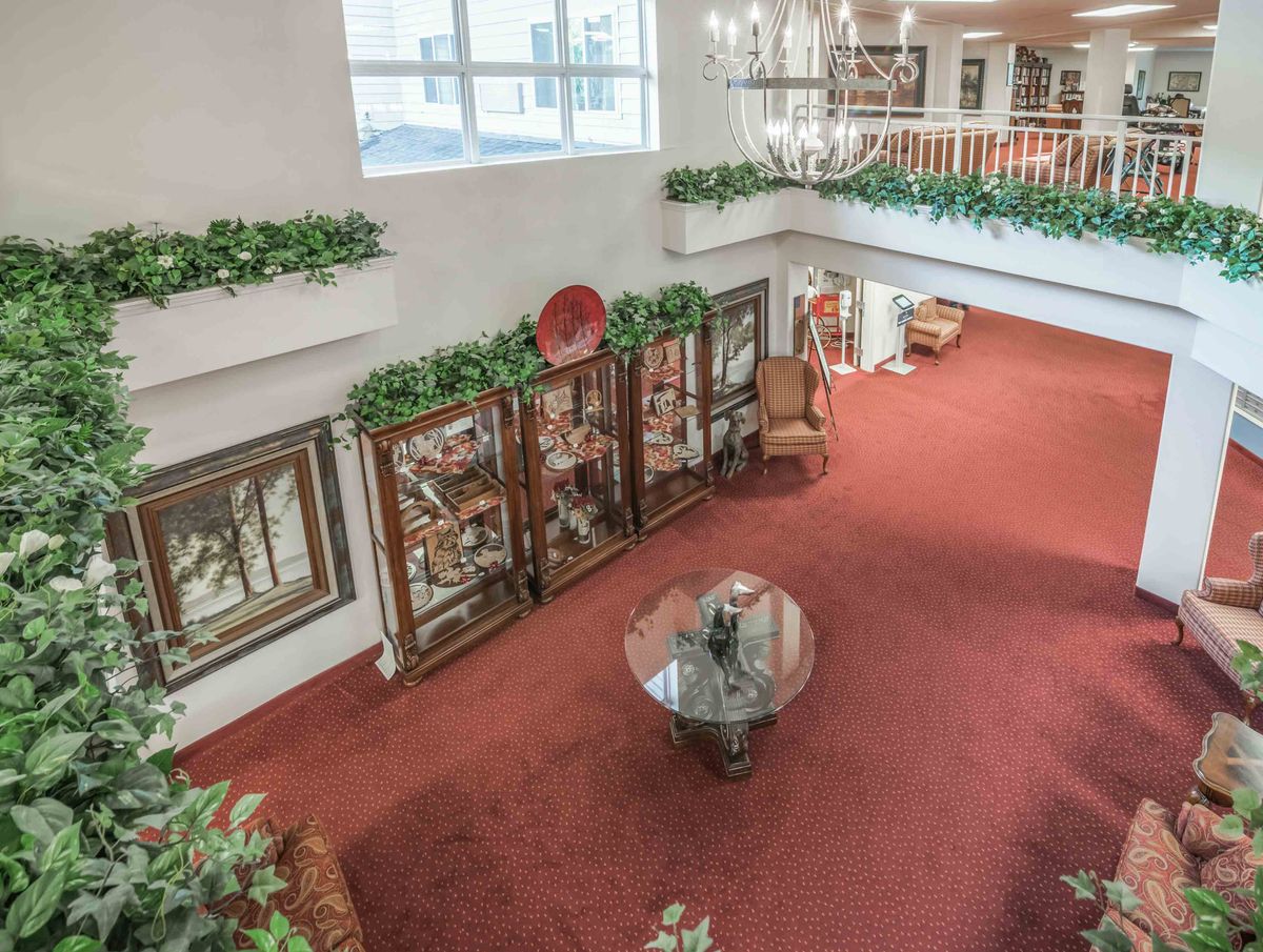 A spacious lobby with red carpeting, decorative plants, and elegant furniture surrounds a glass coffee table.