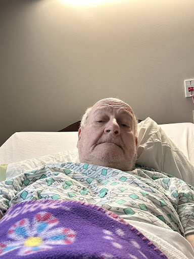 A patient resting in a hospital bed, wearing a medical gown.
