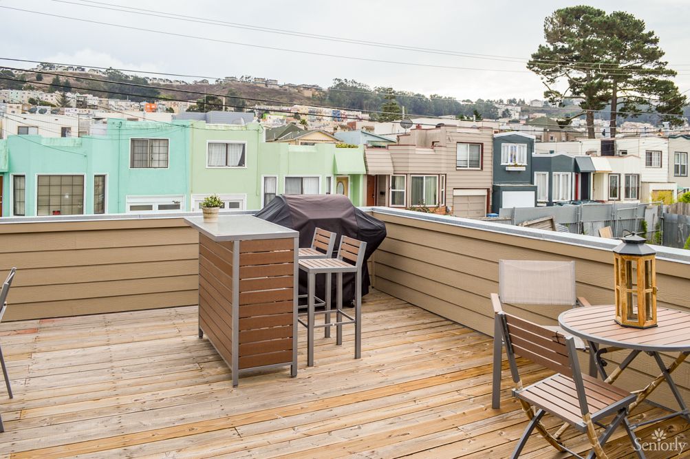 A rooftop deck with outdoor seating and a grill overlooking a residential neighborhood.