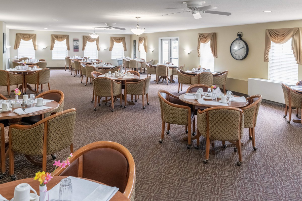 A spacious dining room with neatly arranged tables and chairs, well-lit by large windows.