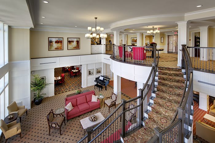 A spacious hotel lobby featuring stylish furniture, a grand staircase, and elegant chandeliers.