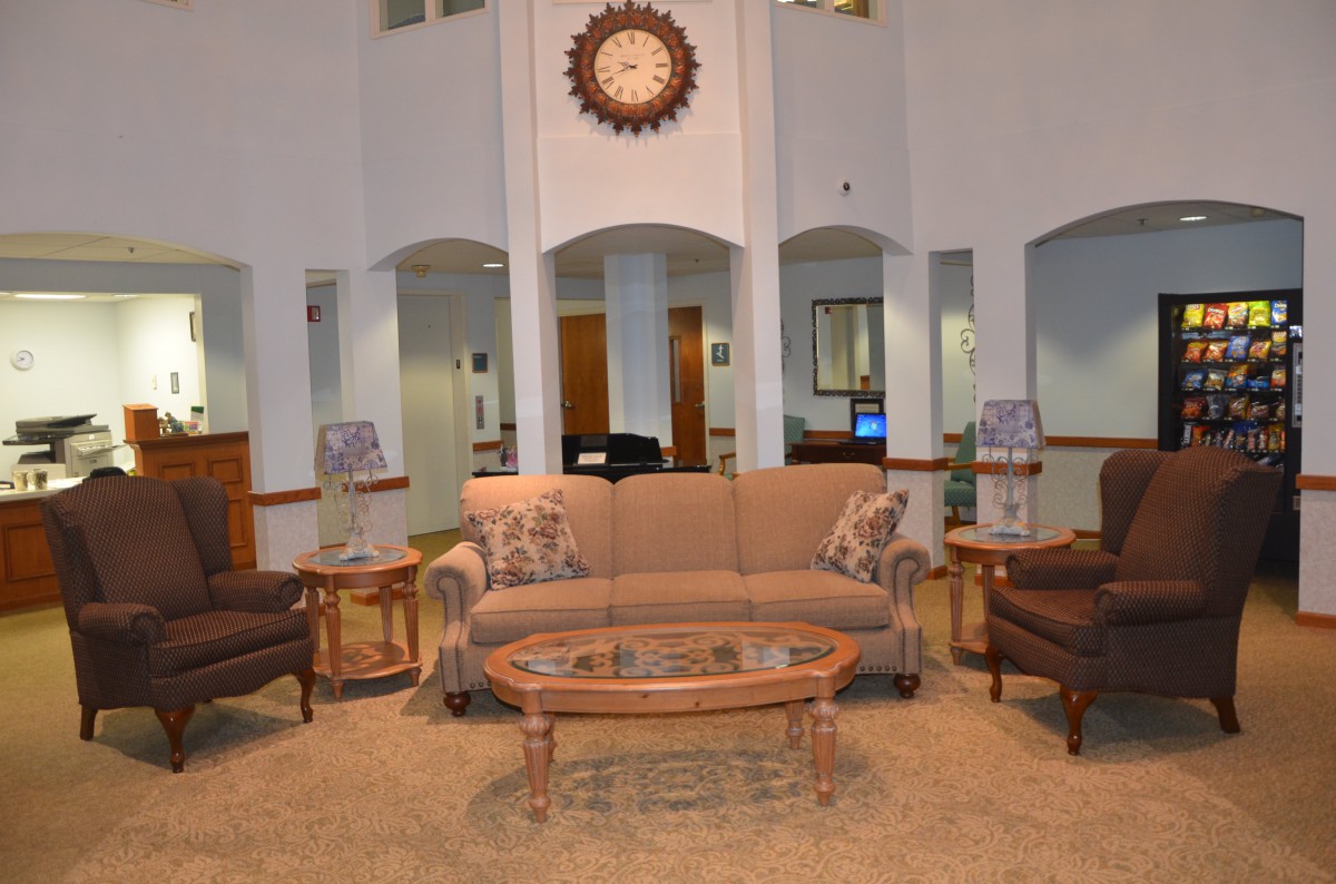 A cozy living room setup featuring a sofa, armchairs, and a glass-top coffee table with a decorative clock on the wall.