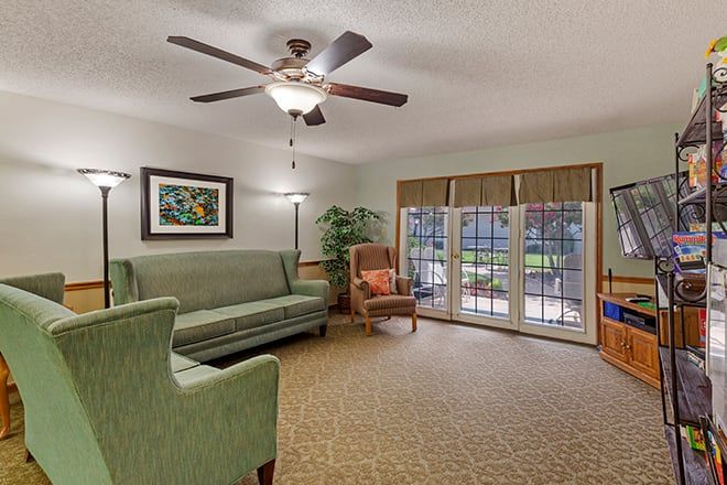 A cozy living room featuring a ceiling fan, sofa, armchair, and large glass doors leading outside.