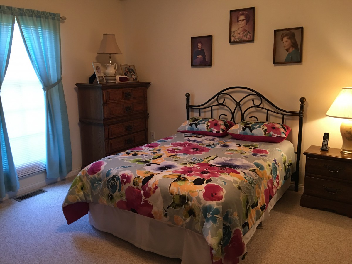 A cozy bedroom with a floral bedspread and decorative portraits on the wall.